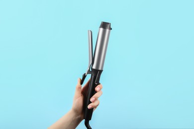 Hair styling appliance. Woman holding curling iron on light blue background, closeup