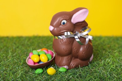Easter celebration. Cute chocolate bunny and half of egg with \candies on grass against yellow background