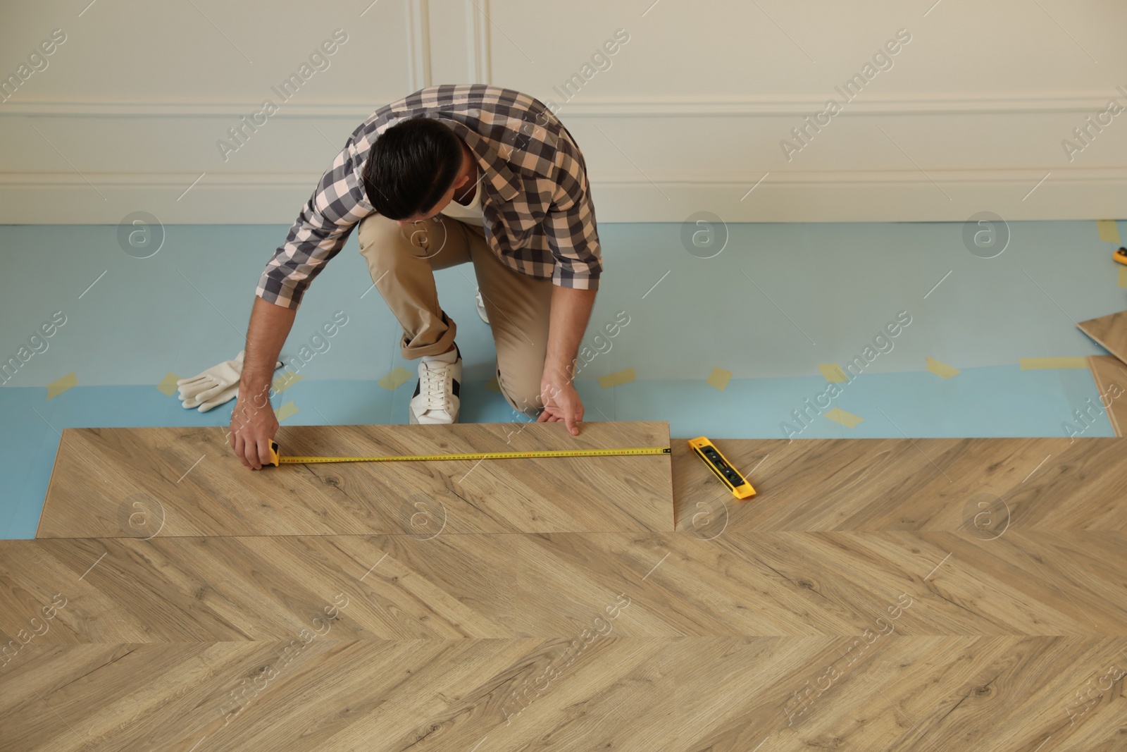 Photo of Professional worker installing new parquet flooring indoors, above view