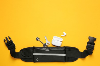 Photo of Stylish black waist bag, keys and earphones on yellow background, flat lay. Space for text