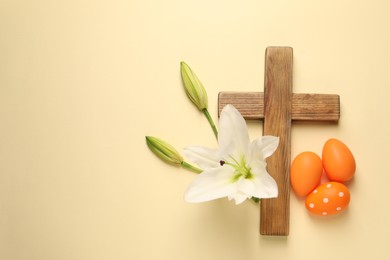 Photo of Wooden cross, painted Easter eggs and lily flowers on pale yellow background, flat lay. Space for text