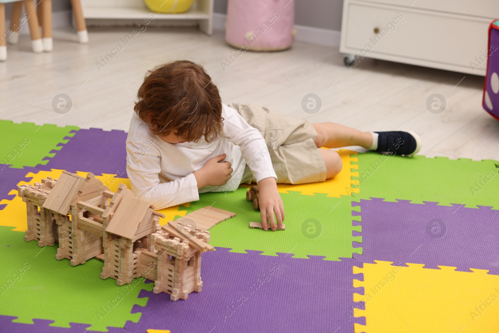 Photo of Little boy playing with wooden construction set on puzzle mat indoors. Child's toy