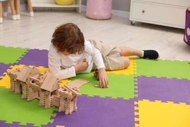 Little boy playing with wooden construction set on puzzle mat indoors. Child's toy