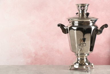 Metal samovar on grey table against pink background, space for text. Russian tea culture