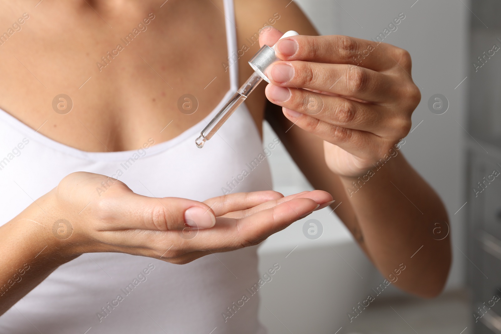 Photo of Woman applying cosmetic serum onto her hand on blurred background, closeup