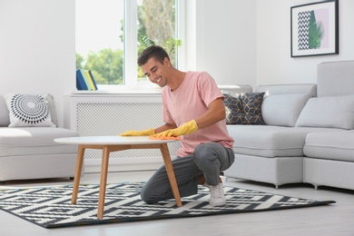 Man cleaning table with rag in living room