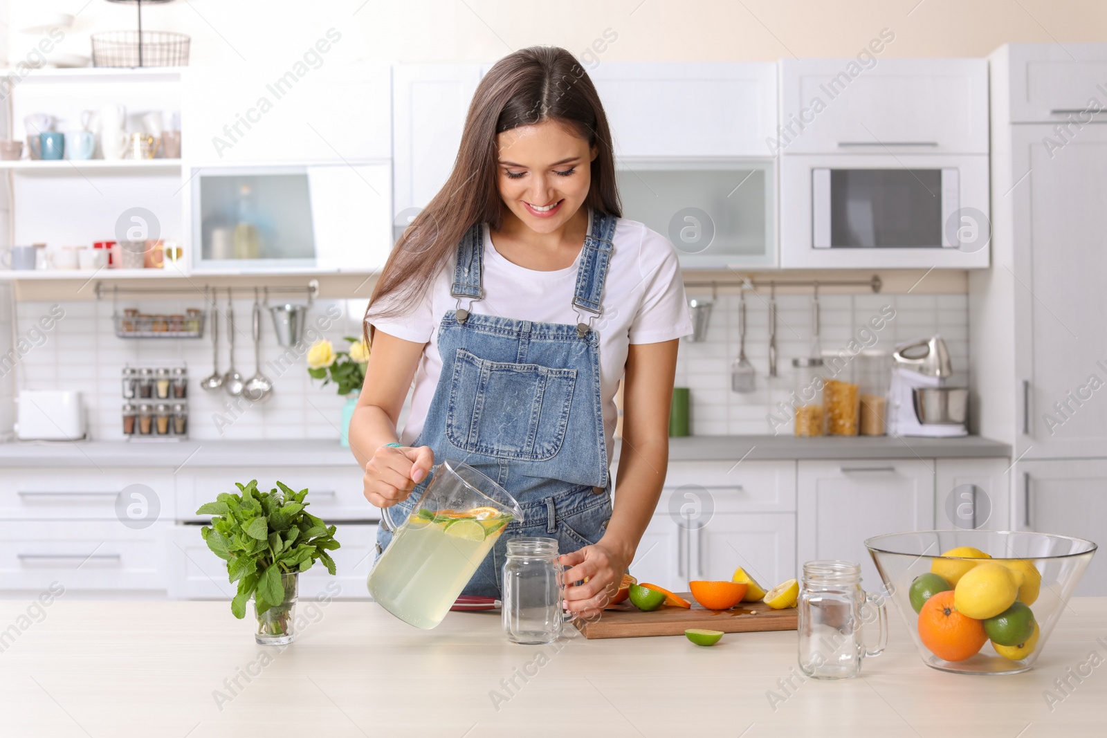 Photo of Young woman preparing lemonade on table in kitchen. Natural detox drink