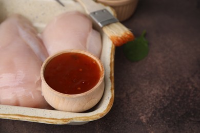 Photo of Marinade, basting brush and raw chicken fillets on brown table, closeup. Space for text