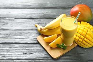 Photo of Tasty tropical drink with mango and fresh fruits on wooden table. Space for text