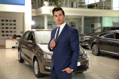 Photo of Young salesman near new car in modern dealership