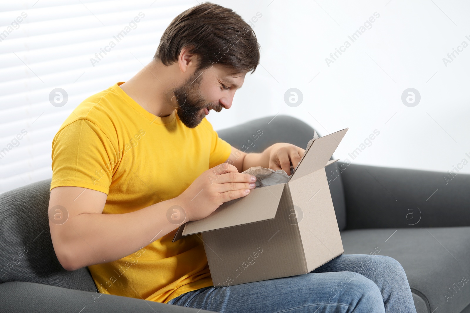 Photo of Happy man opening parcel at home. Internet shopping