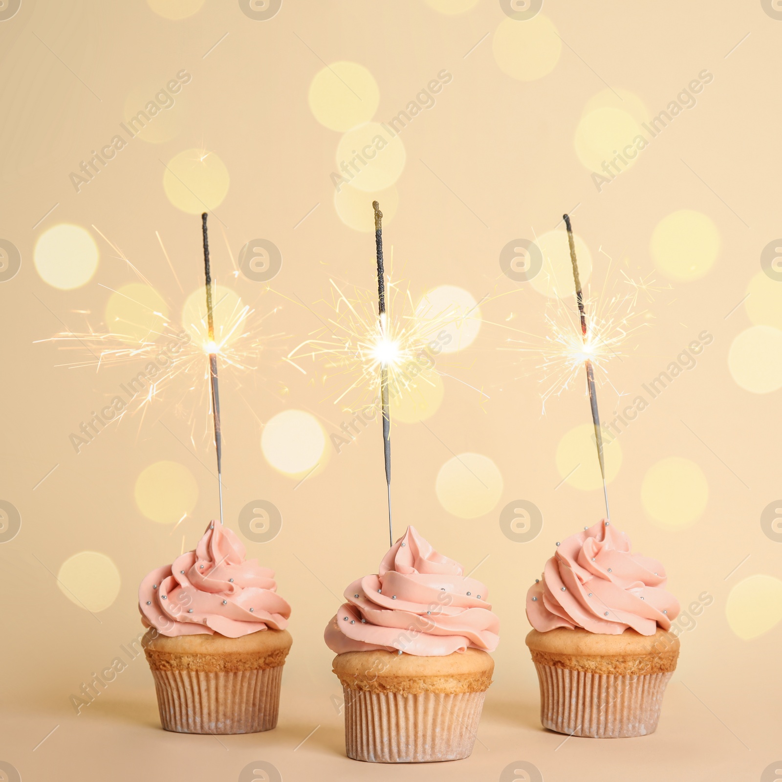 Image of Birthday cupcakes with sparklers on beige background