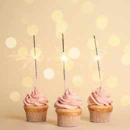 Image of Birthday cupcakes with sparklers on beige background