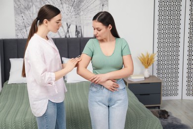 Woman giving insulin injection to her diabetic friend in bedroom