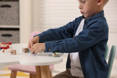 Photo of Little boy playing with wooden pieces and string for threading activity at white table indoors, closeup. Child's toy