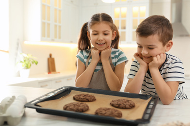 Cute little children with fresh delicious cookies in kitchen. Cooking together
