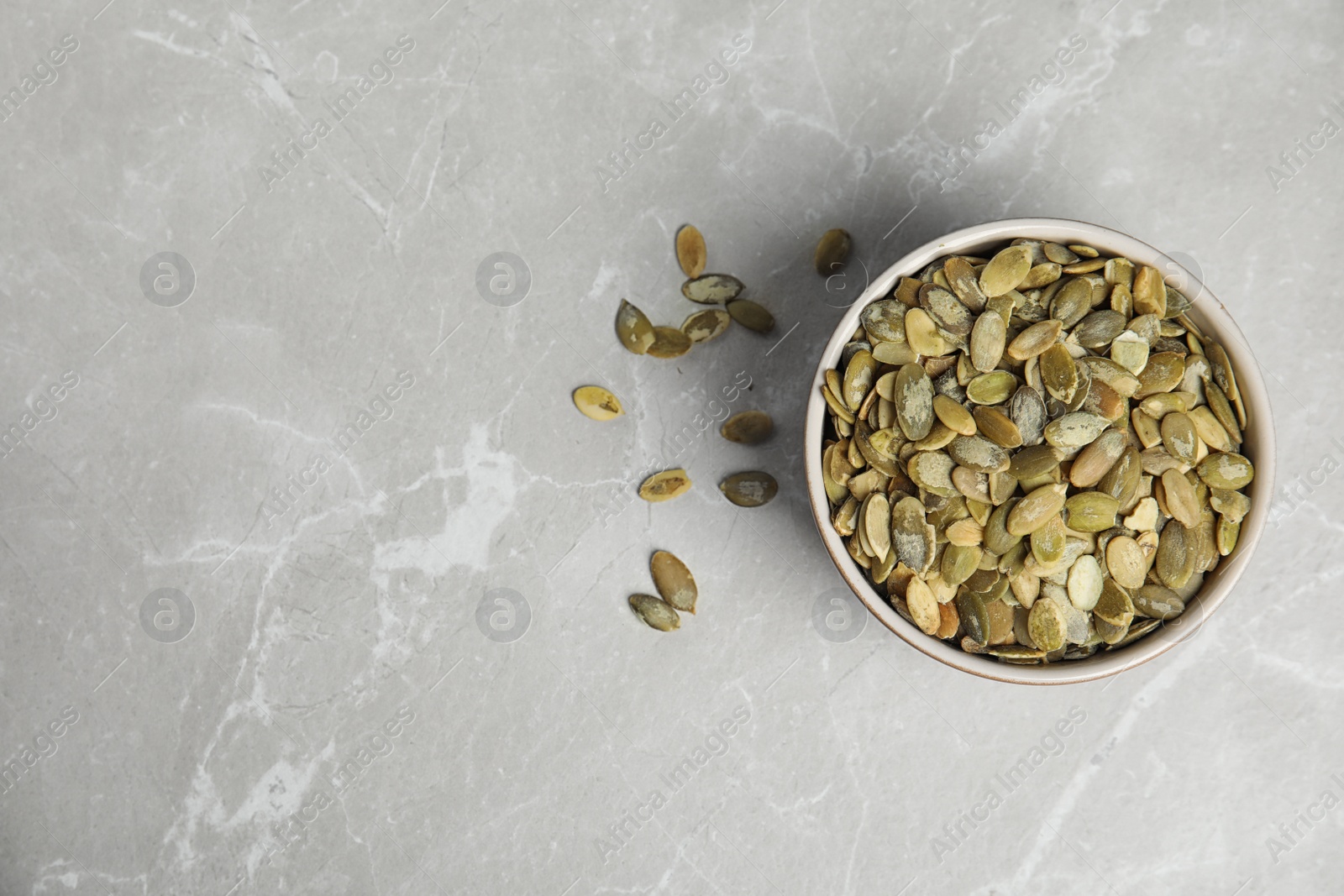 Photo of Bowl of raw pumpkin seeds on light grey marble table, top view. Space for text