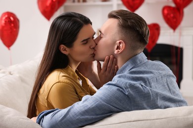 Photo of Lovely couple kissing on sofa indoors. Valentine's day celebration