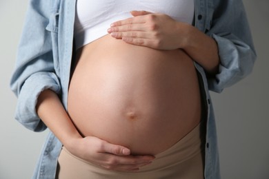 Photo of Pregnant woman touching her belly on light grey background, closeup