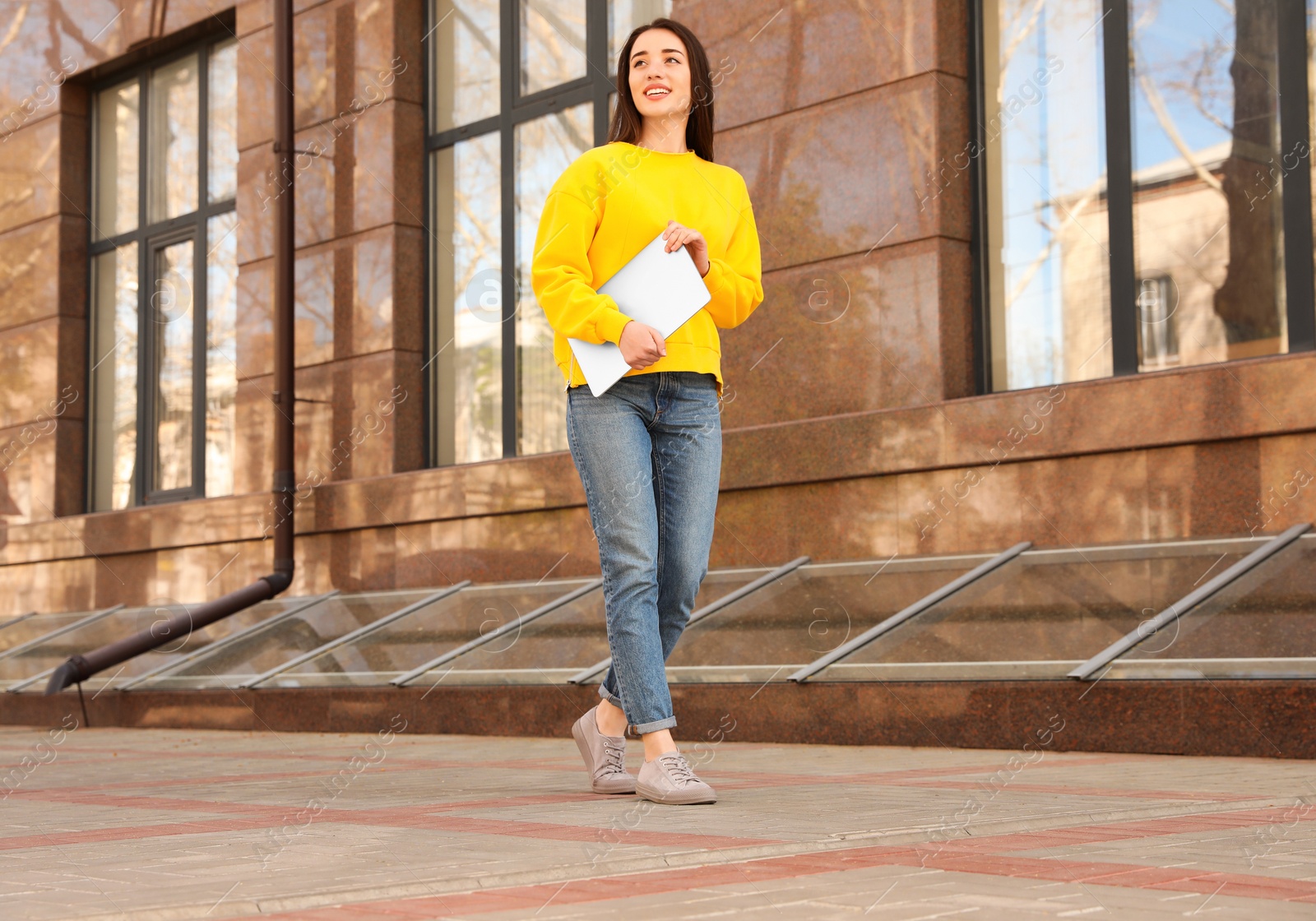 Image of Happy young woman with laptop walking outdoors