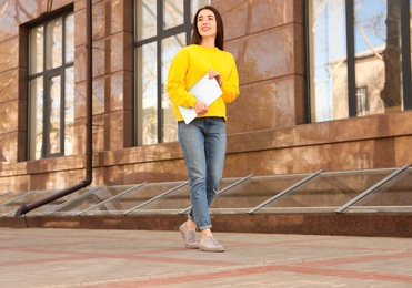 Happy young woman with laptop walking outdoors