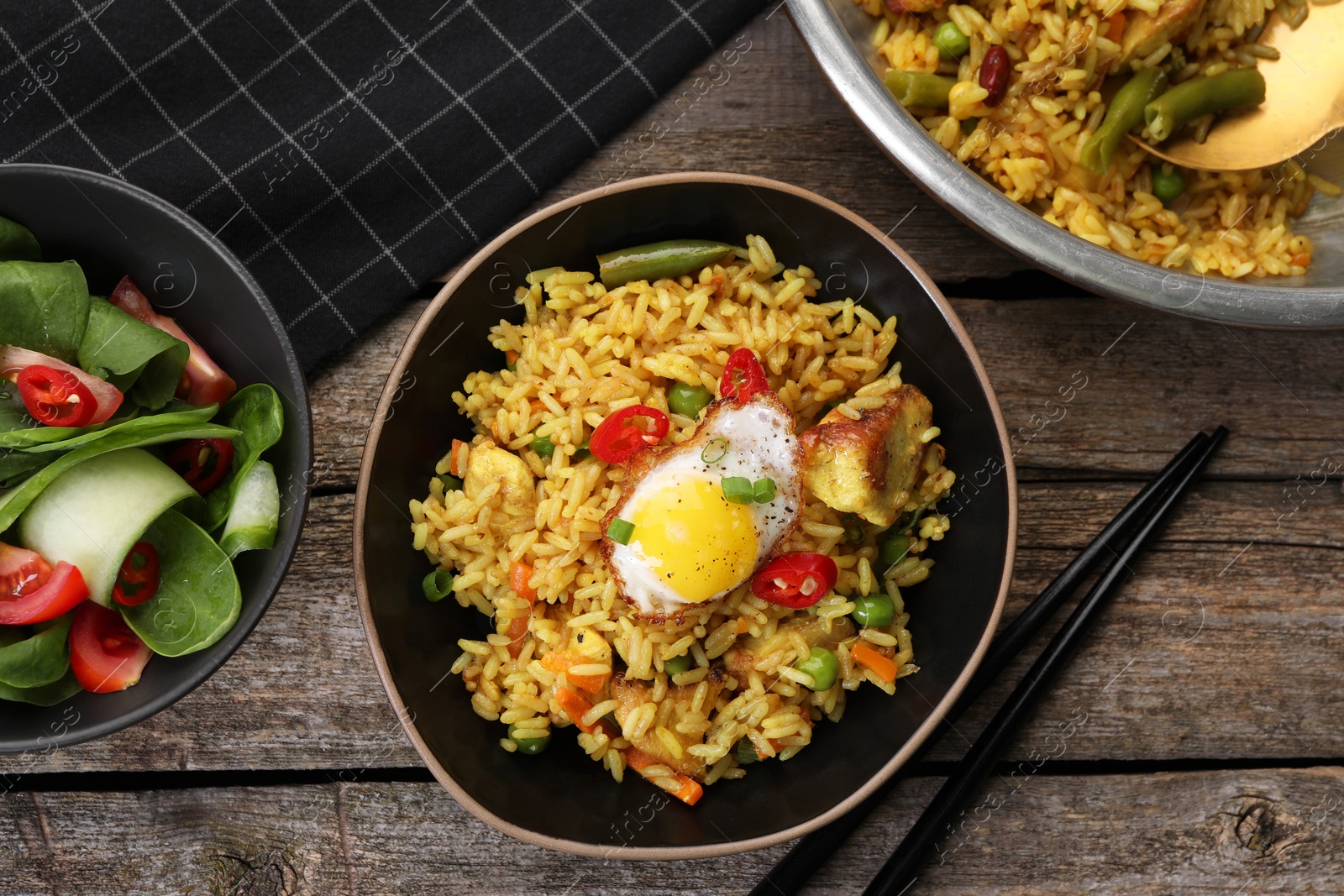 Photo of Tasty rice with meat, egg and vegetables in bowl served on wooden table, flat lay