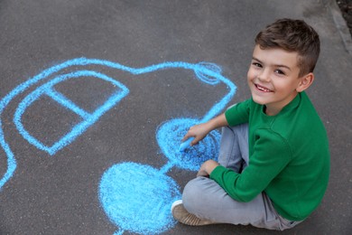 Child drawing car with chalk on asphalt