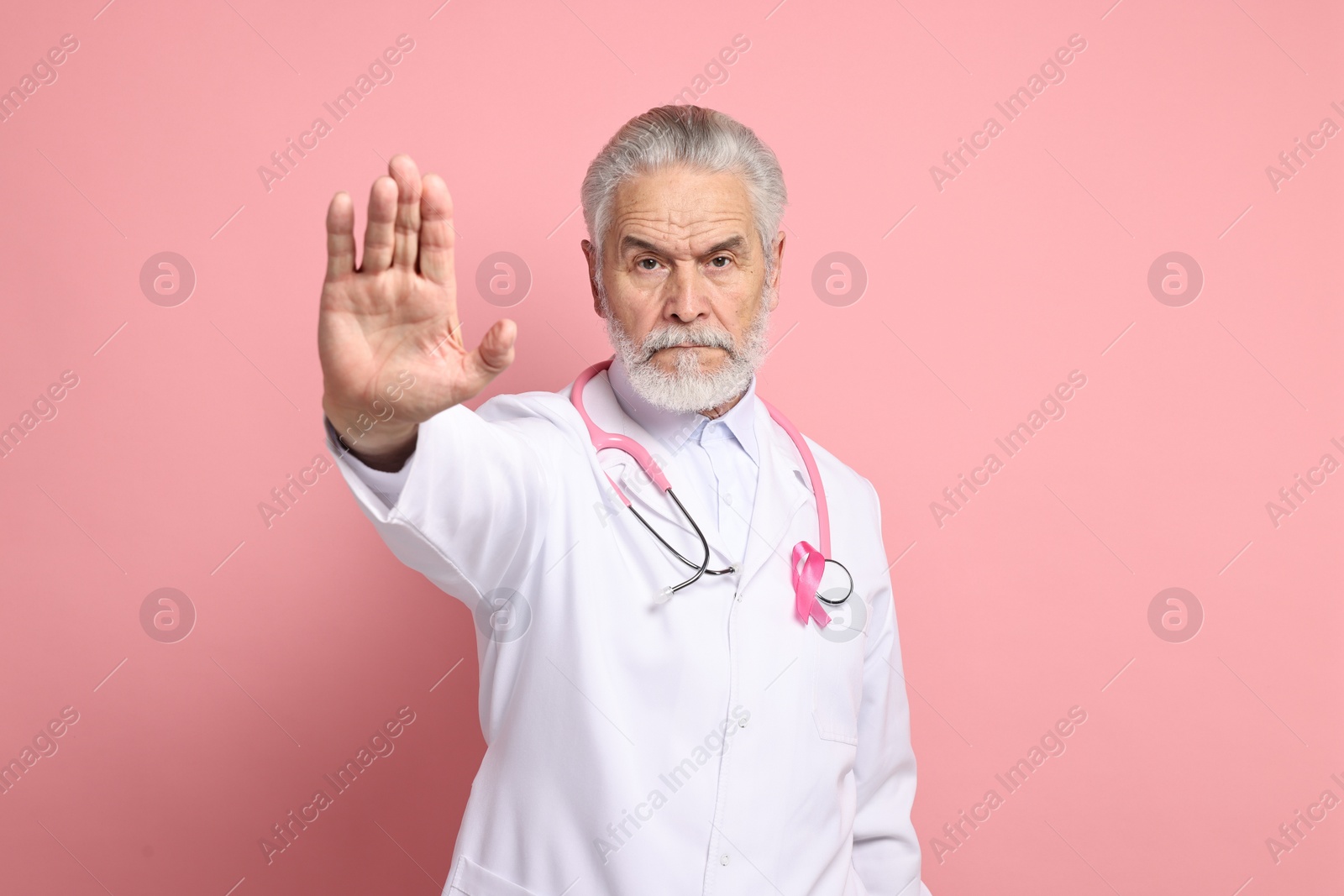 Photo of Mammologist with pink ribbon showing stop gesture on color background. Breast cancer awareness