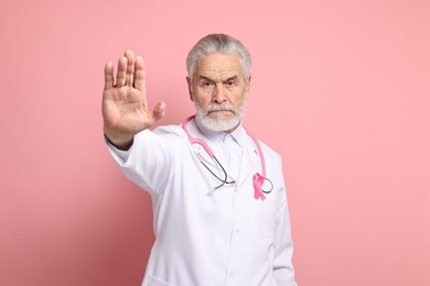 Photo of Mammologist with pink ribbon showing stop gesture on color background. Breast cancer awareness