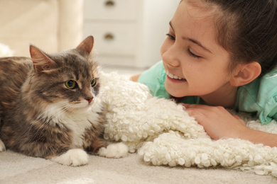 Photo of Cute little girl with cat lying on carpet at home. First pet