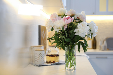 Photo of Beautiful peonies in vase on kitchen counter