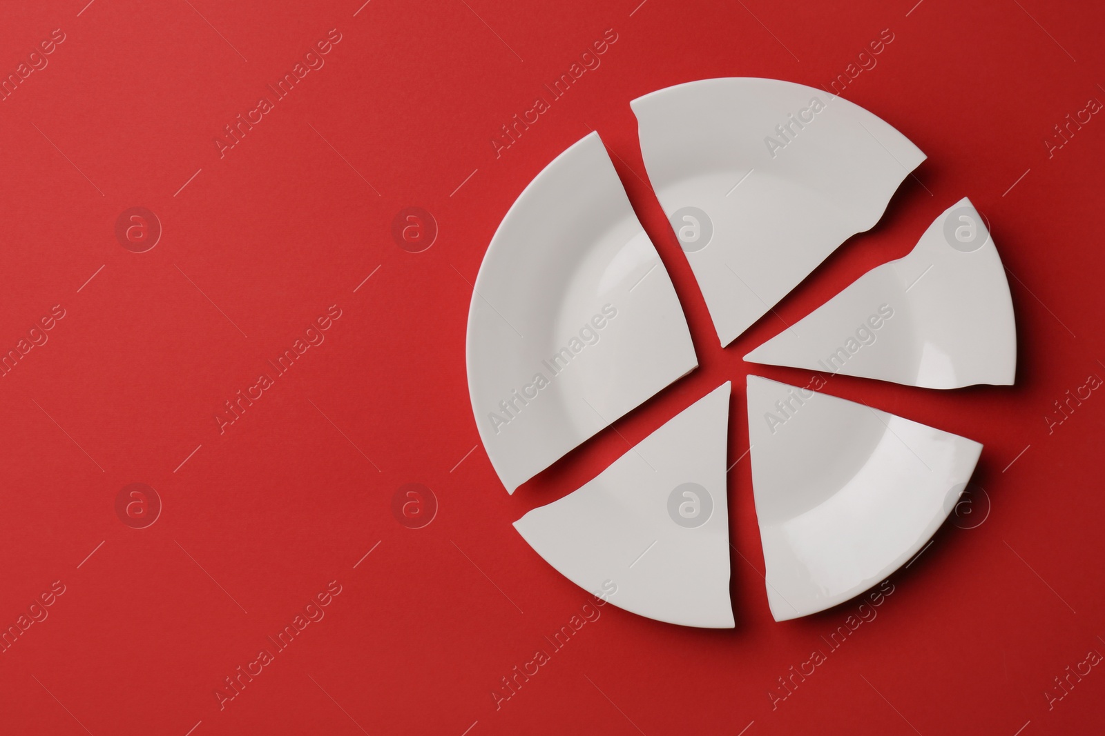 Photo of Pieces of broken white ceramic plate on red background, top view. Space for text