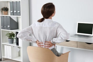 Photo of Woman suffering from back pain while sitting in office. Symptom of scoliosis