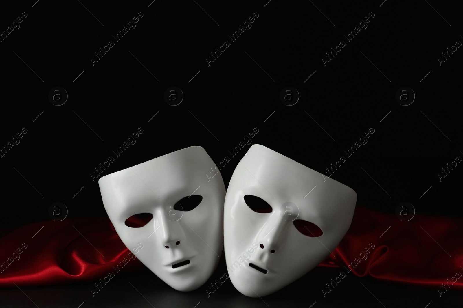 Photo of White theatre masks and red fabric on black background