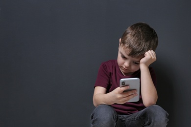 Photo of Sad little boy with mobile phone on black background, space for text