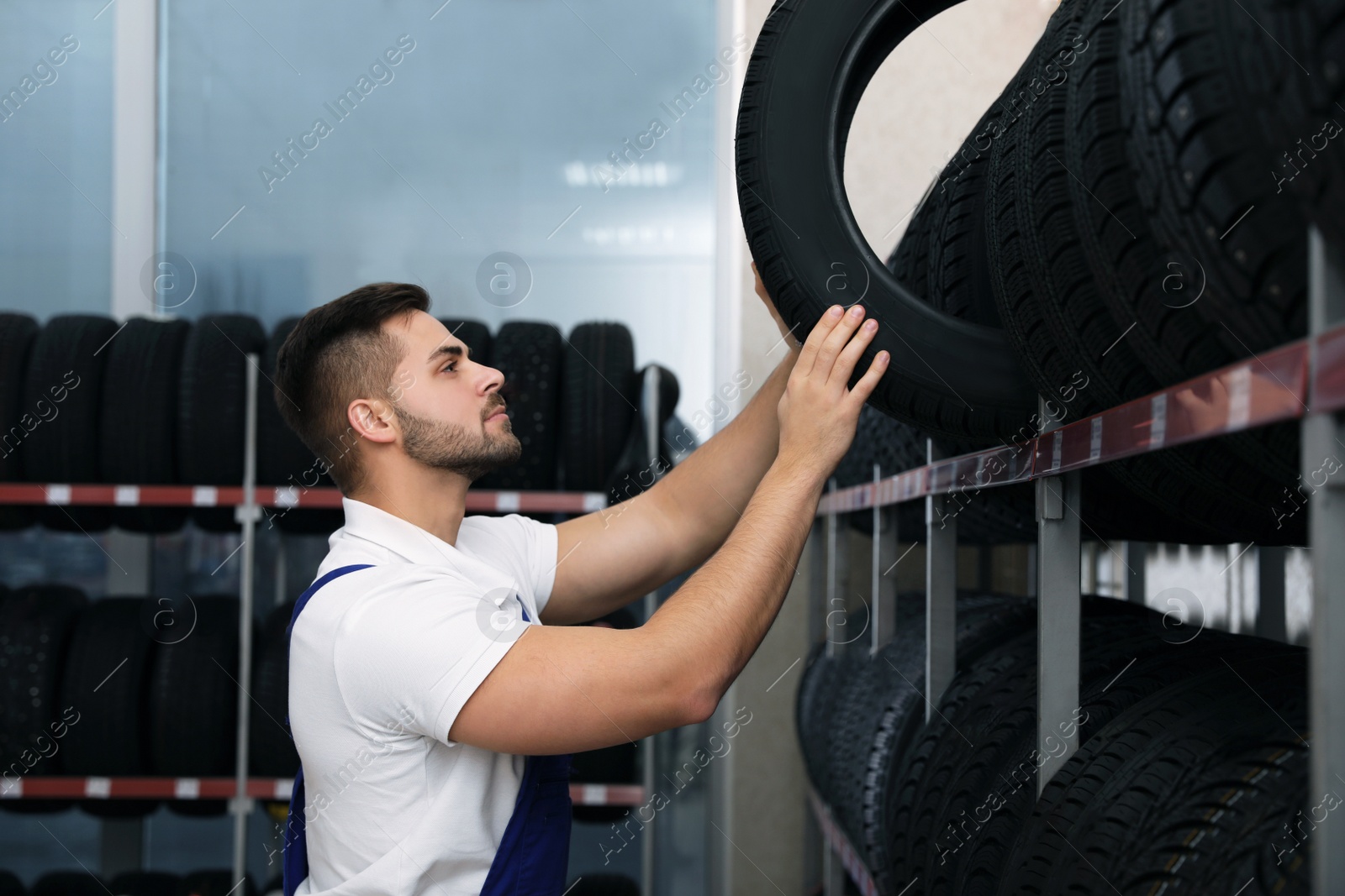 Photo of Male mechanic with car tire in auto store