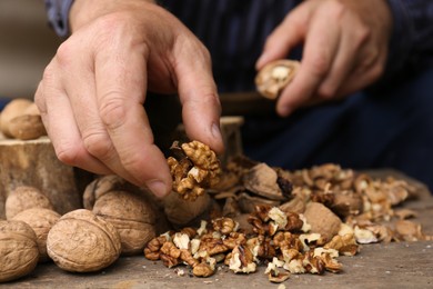 Photo of Man cracking walnuts at wooden table, closeup
