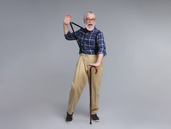 Cheerful senior man with walking cane on gray background
