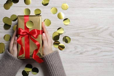 Photo of Christmas present. Woman with gift box and confetti on white wooden background, top view. Space for text