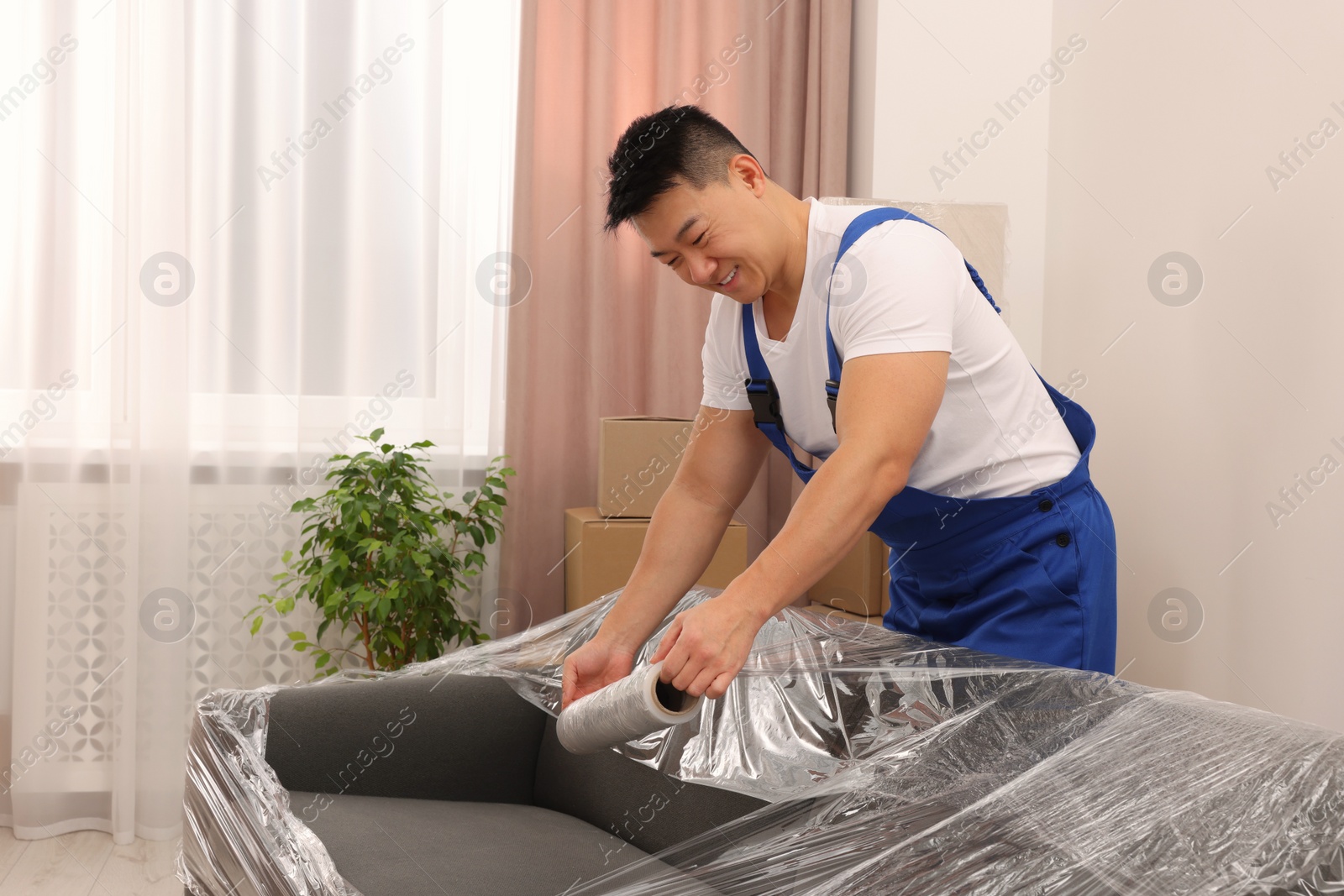 Photo of Worker wrapping sofa in stretch film indoors