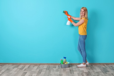 Photo of Woman in gloves cleaning color wall with sponge