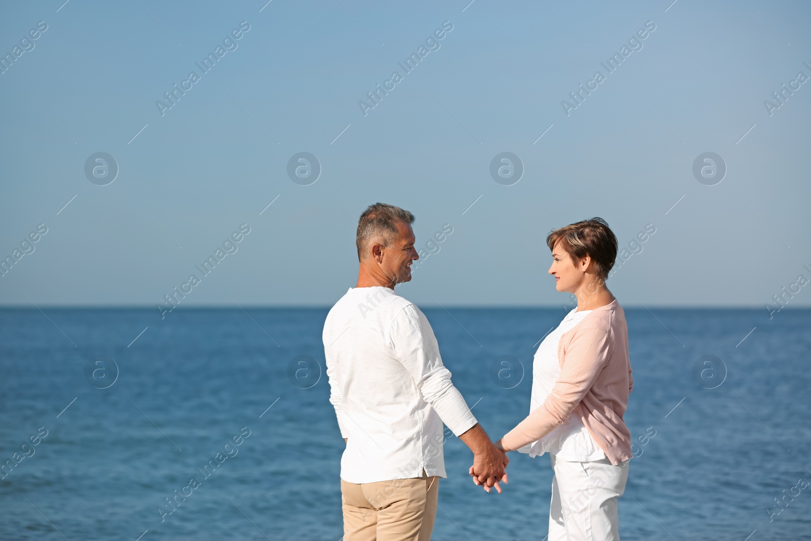 Photo of Happy mature couple holding hands at beach on sunny day