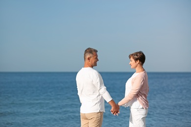 Happy mature couple holding hands at beach on sunny day