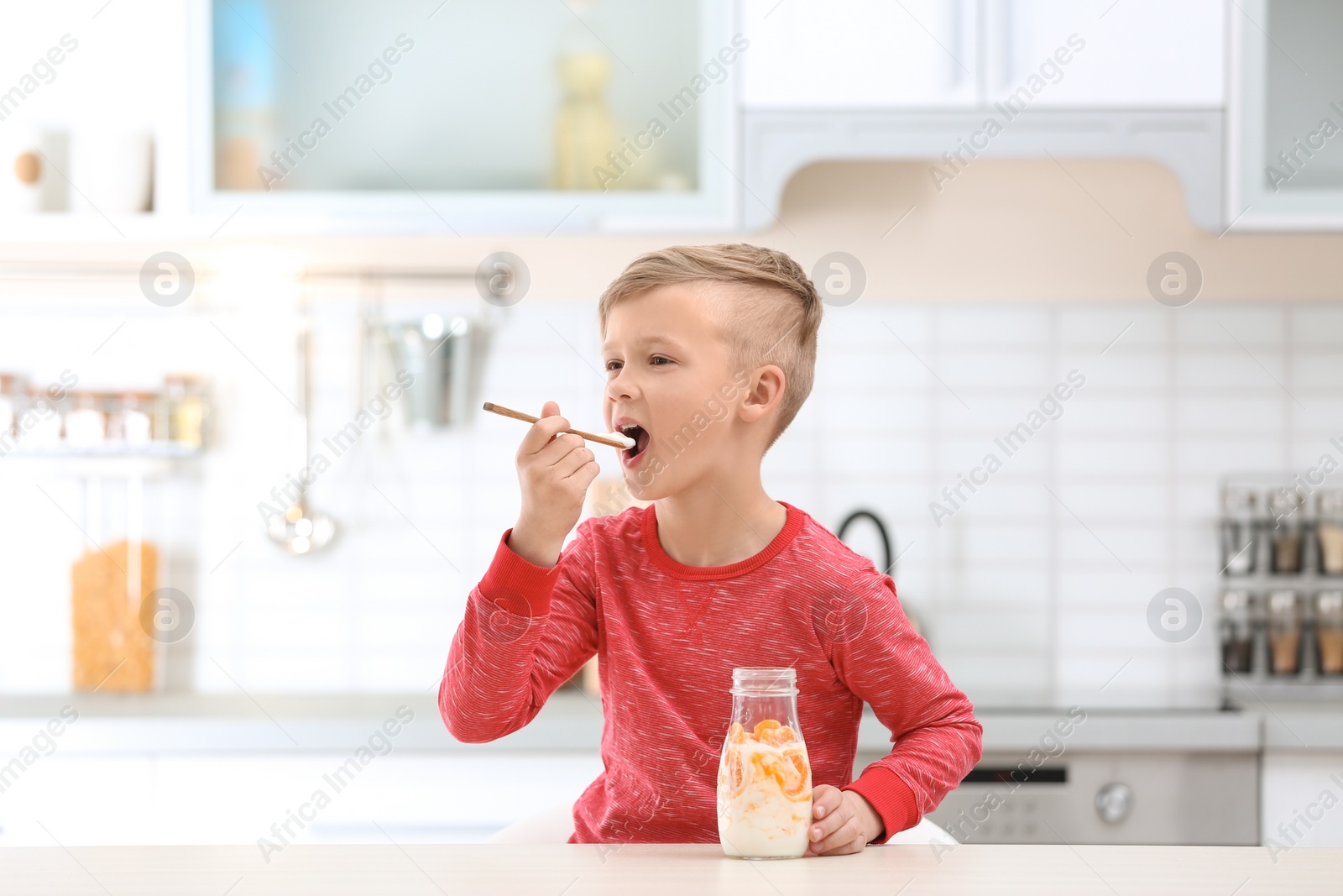 Photo of Little boy with yogurt in kitchen