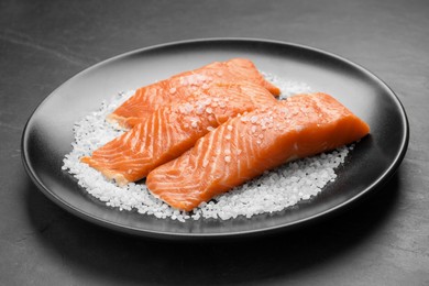Photo of Fresh raw salmon with salt on black table, closeup