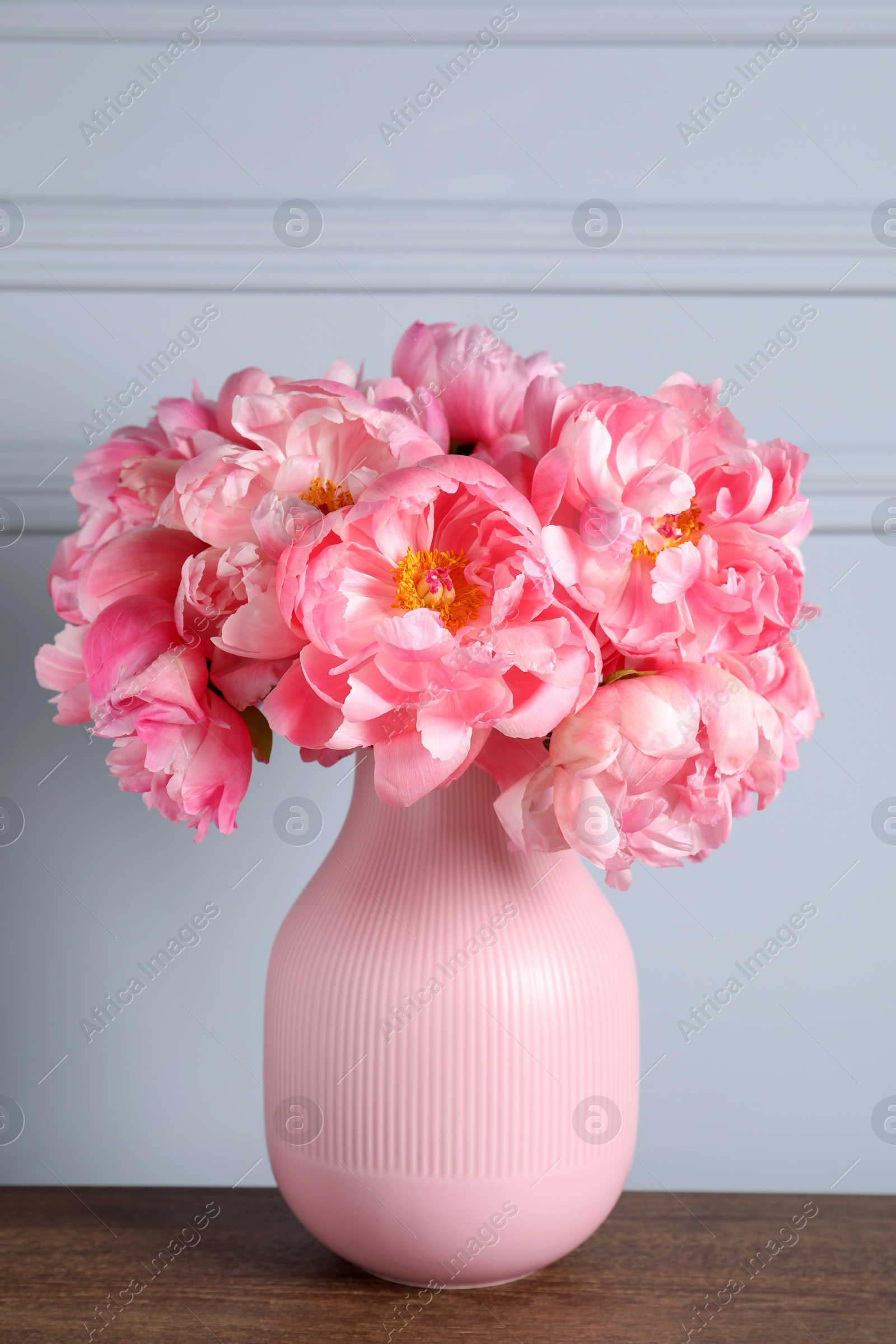 Photo of Beautiful bouquet of pink peonies in vase on wooden table near grey wall