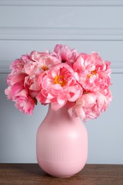 Beautiful bouquet of pink peonies in vase on wooden table near grey wall