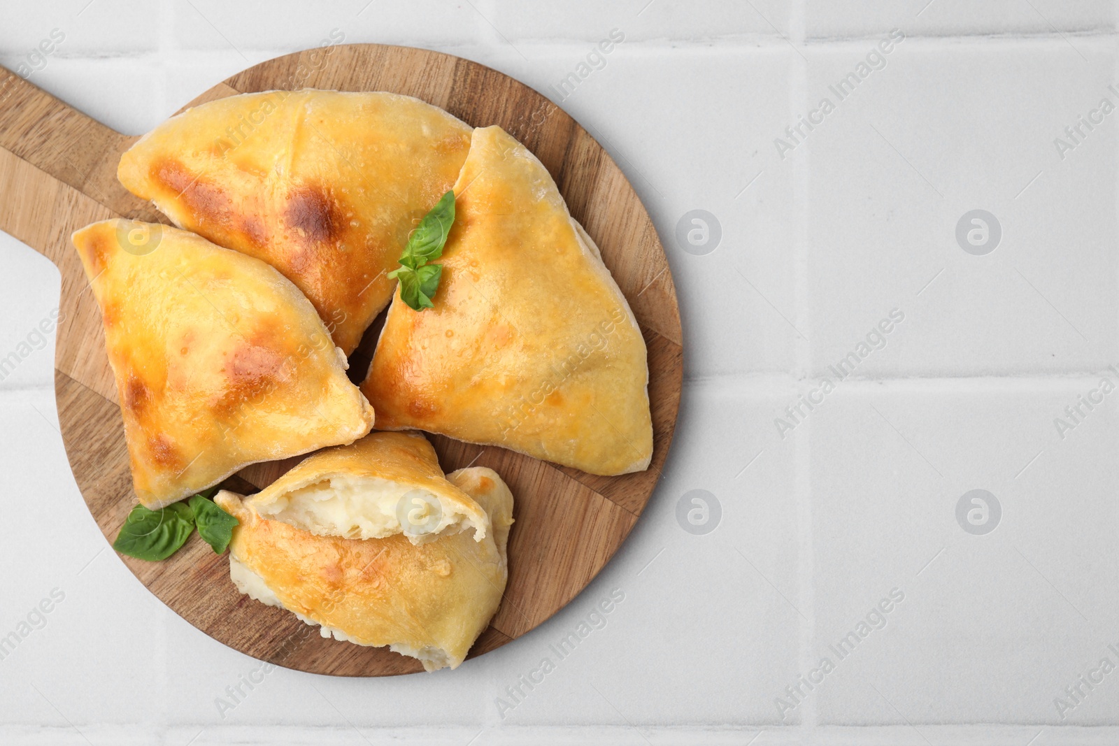 Photo of Delicious samosas and basil on white tiled table, top view. Space for text