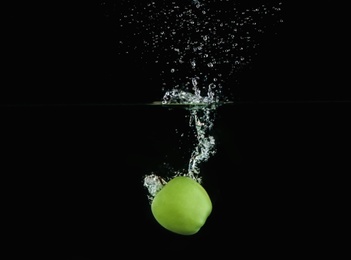 Photo of Ripe green apple falling down into clear water with splashes against black background