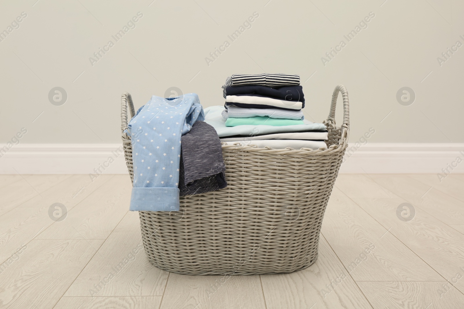 Photo of Wicker basket with folded clothes on floor in room